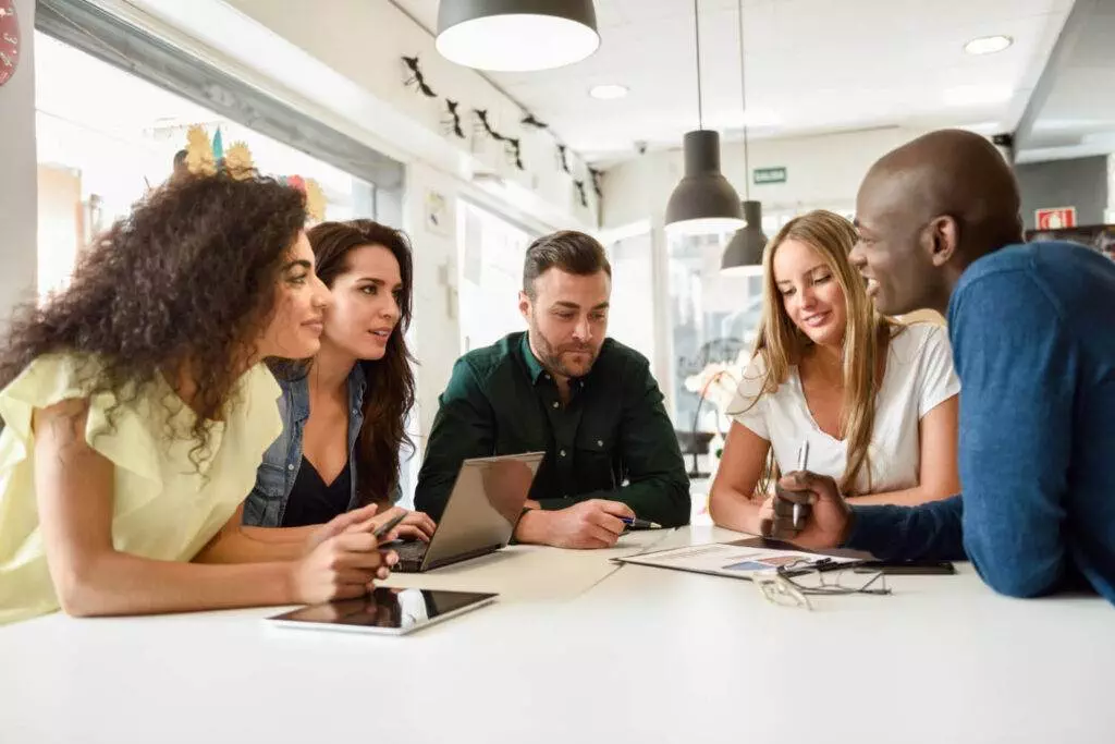 Multi ethnic group of young people studying together on white desk